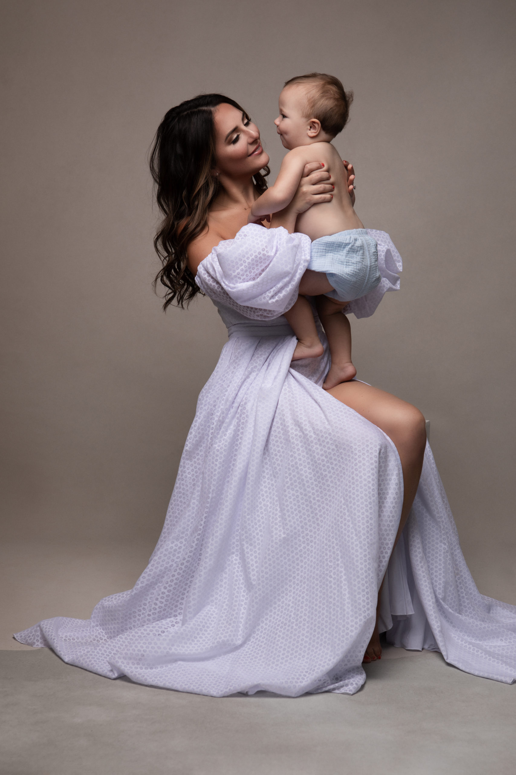 new mom holding her baby in the air while wearing a purple maternity gown