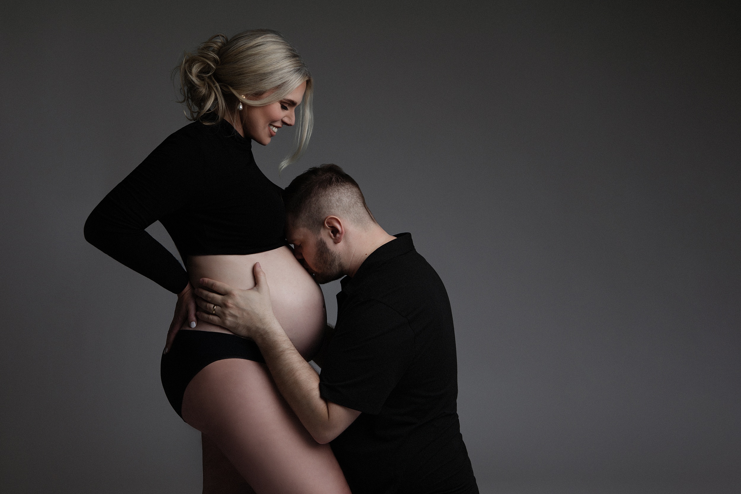 mom to be with her husband kissing her baby bump atlanta midwives