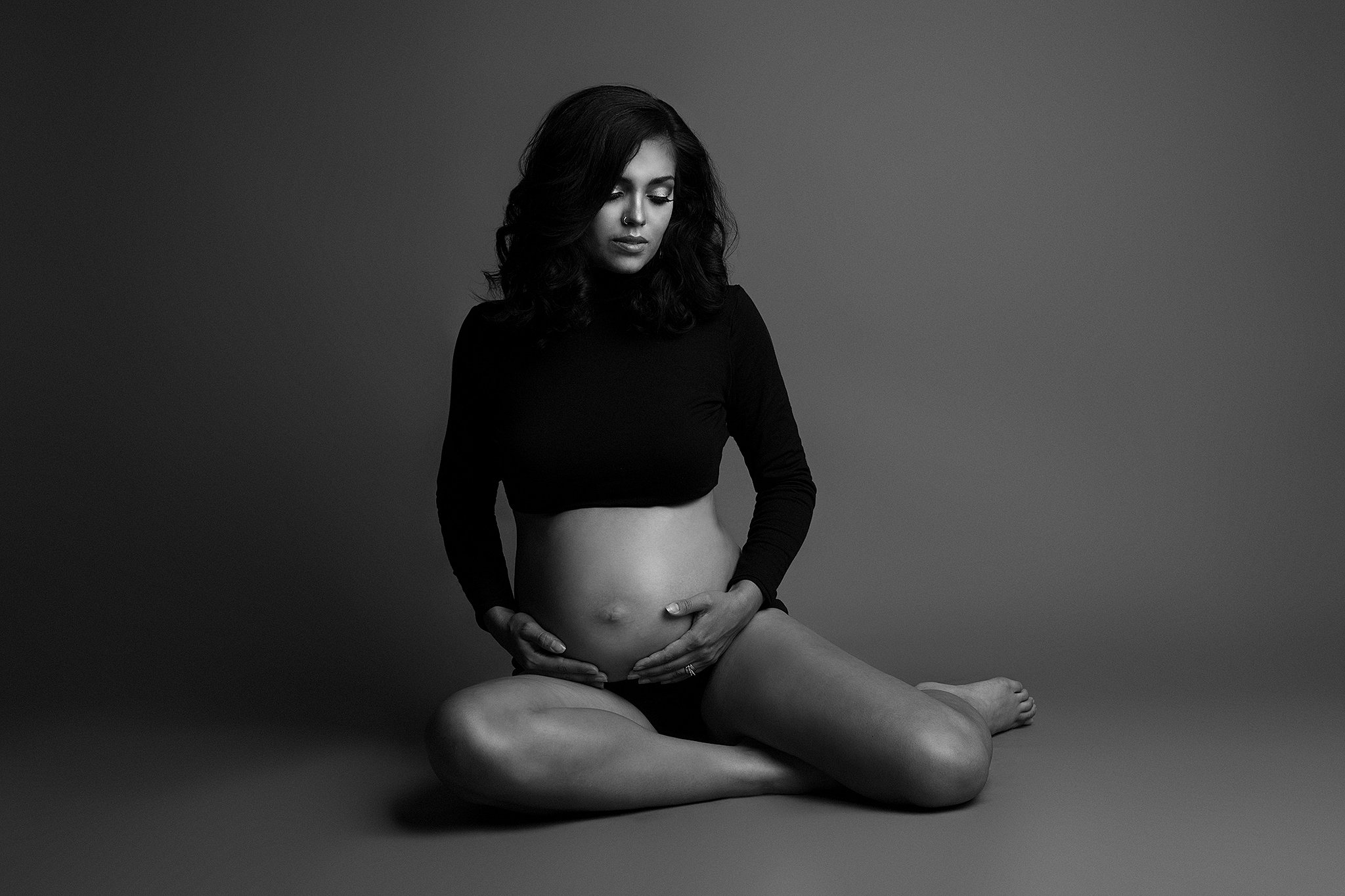 pregnant woman in black long sleeve crop top sitting on the floor cradling her bump Bayshore Womens Healthcare