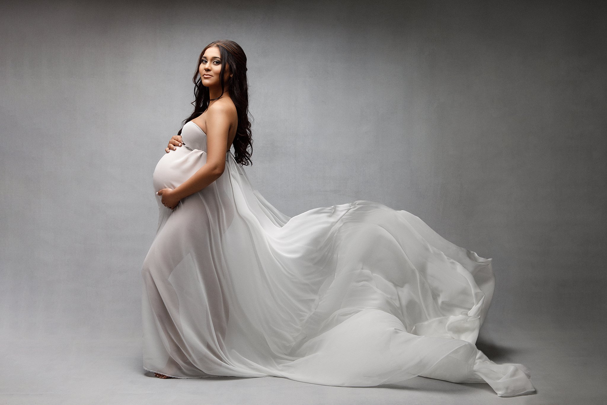 pregnant woman in white gown with her leg popped and holding her bump