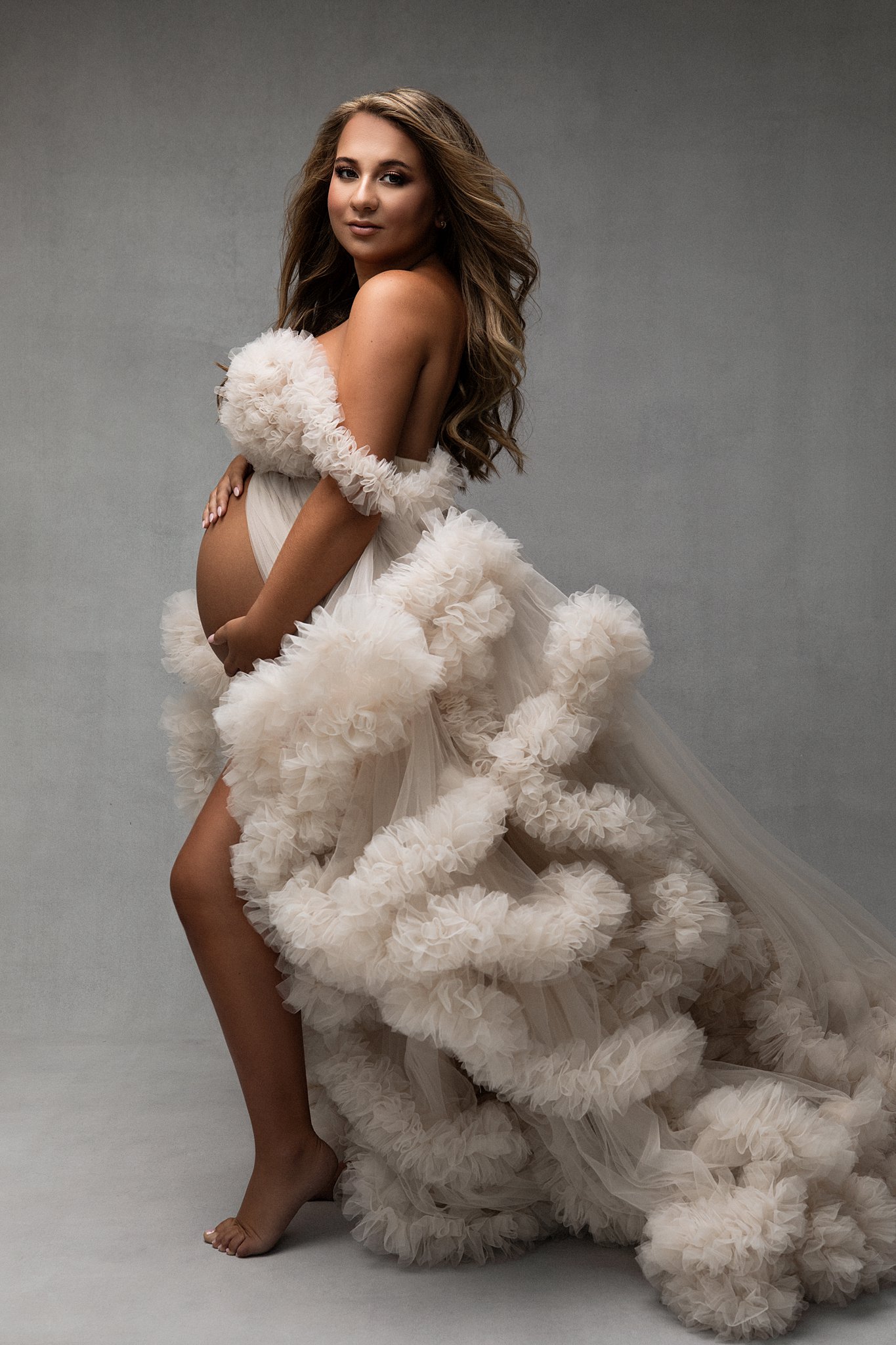 mom to be in a tan tulle gown holding her bump