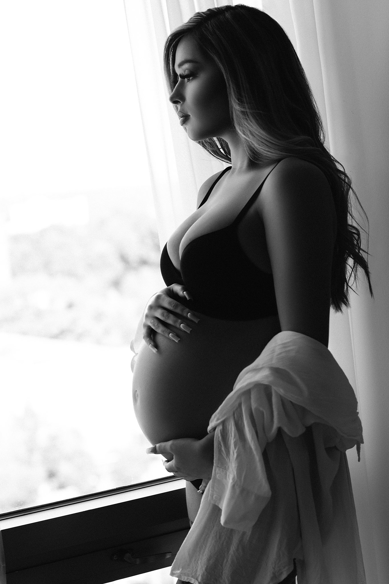 mom to be looks out a window while holding her bump Atlanta gynecology
