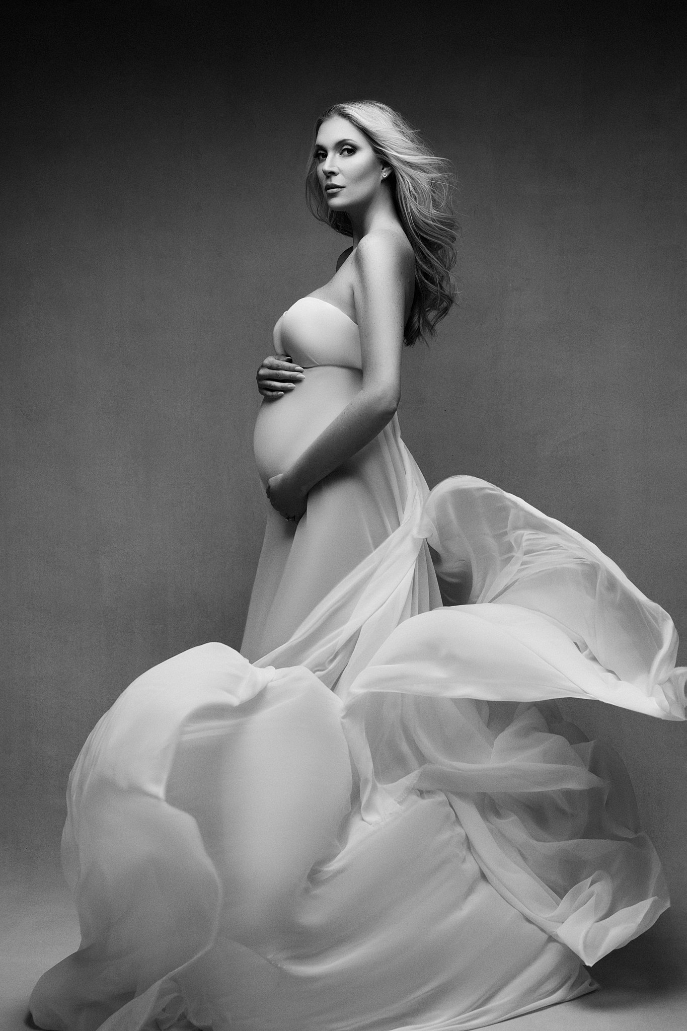 mom to be holds her bump while her long maternity gown flows around her Dawning life midwifery