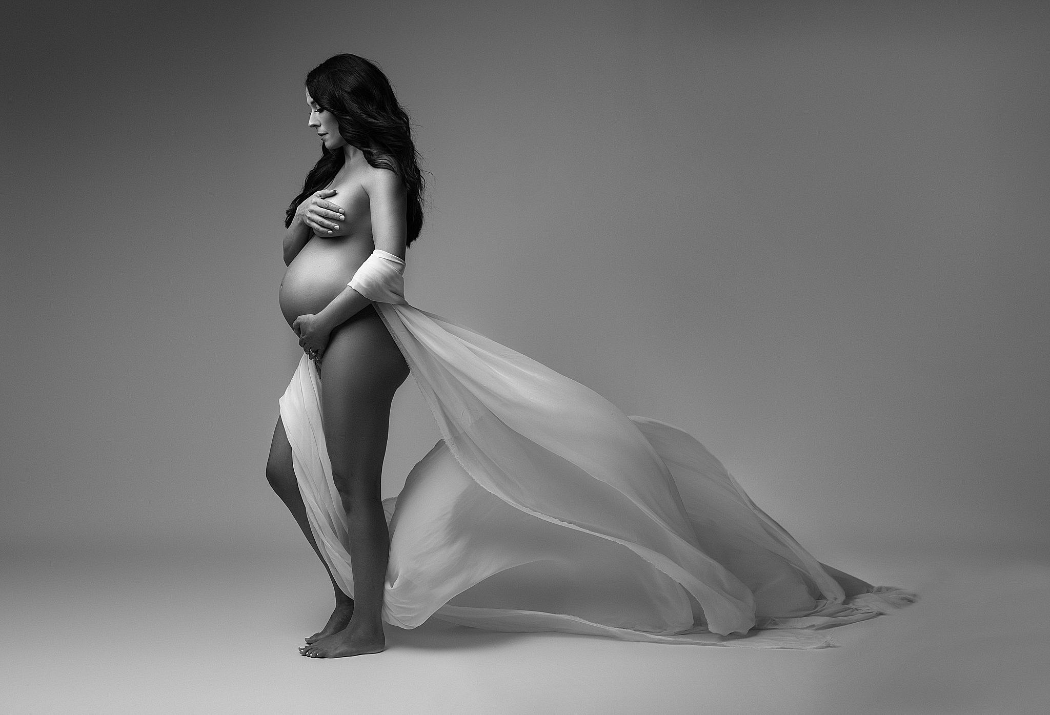 Mom to be holds her bump with a long flowing fabric in a studio Miami Beach Community Health Center