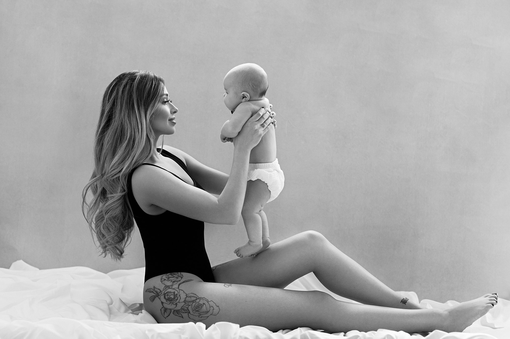 woman sits in a studio in a one piece holding her newborn in front of her Miami interior decorator