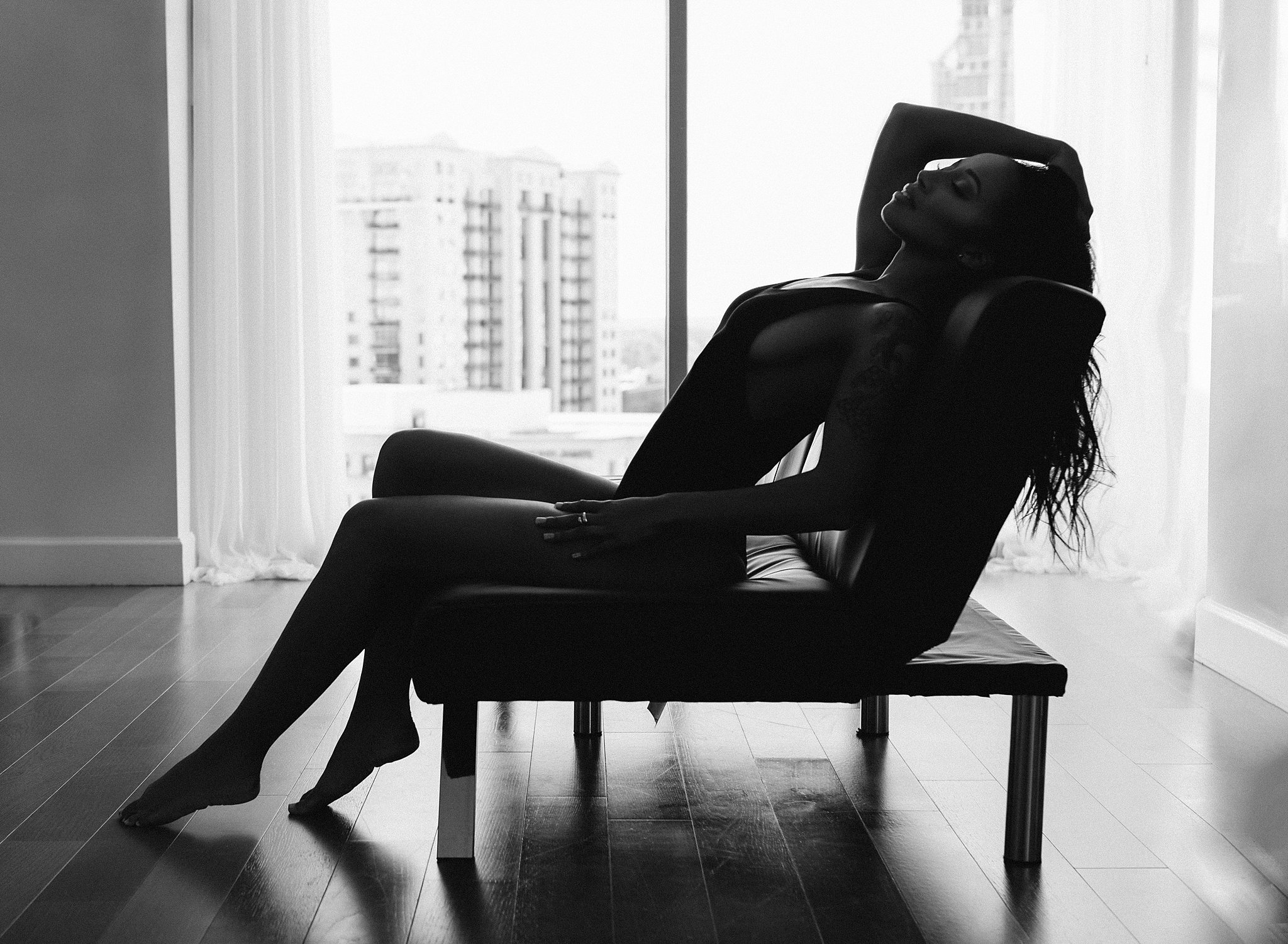 silhouette of a woman leaning back on leather couch in black swimsuit omg miami swimwear