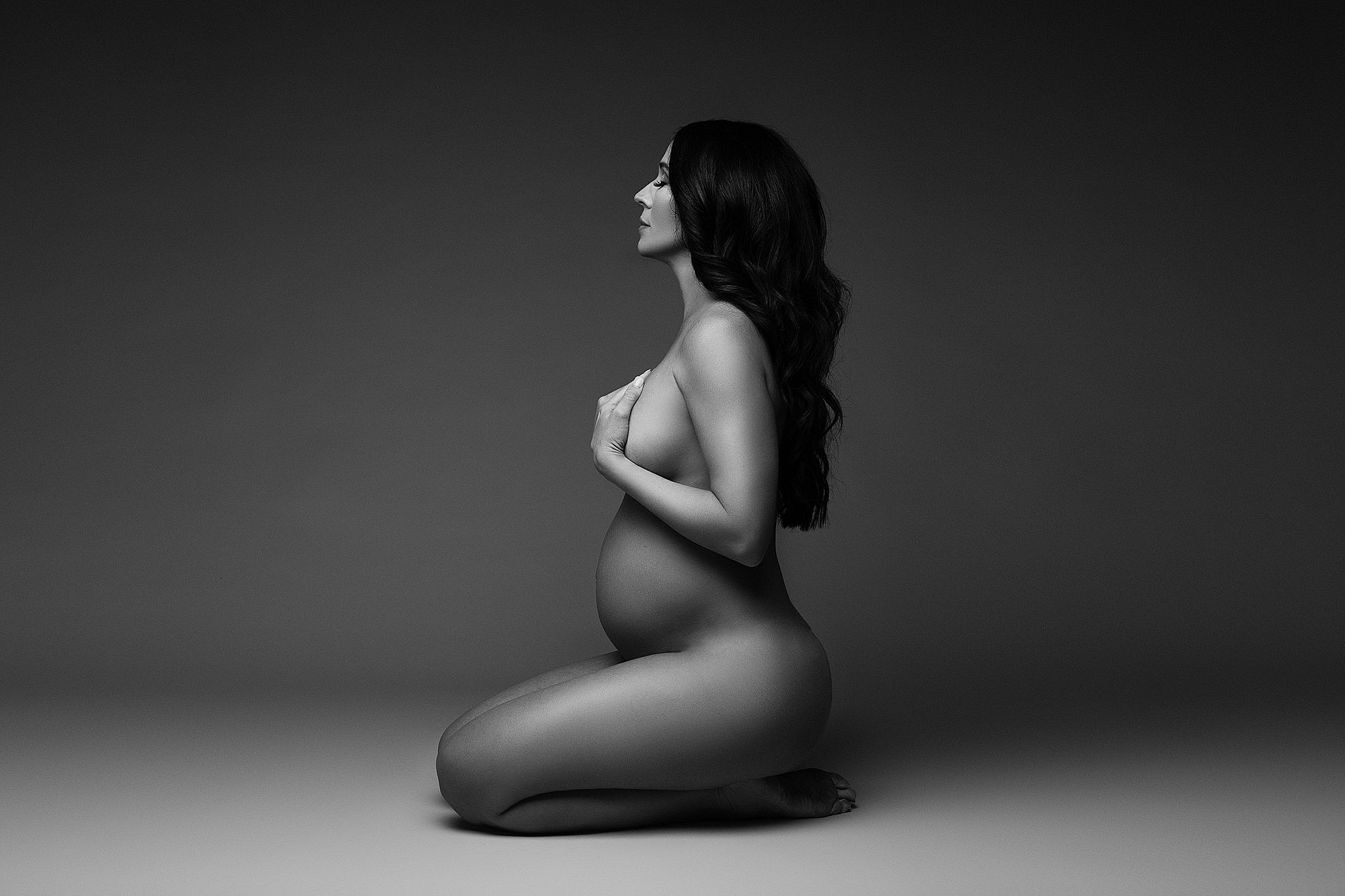 pregnant woman kneeling on the ground covering her breasts