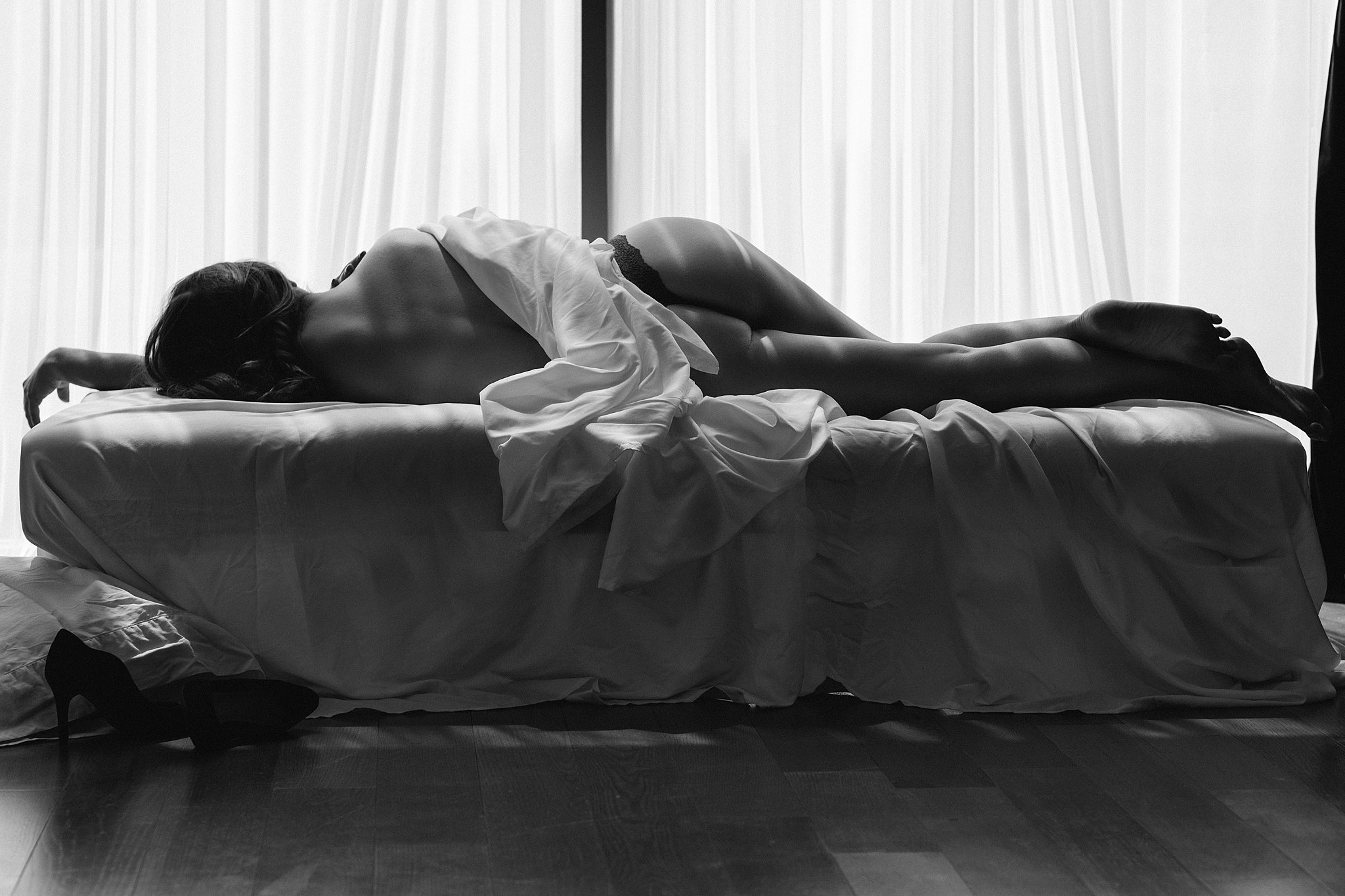 woman lays on her side on a small bed by a window wearing black lingerie the spa at mandarin oriental