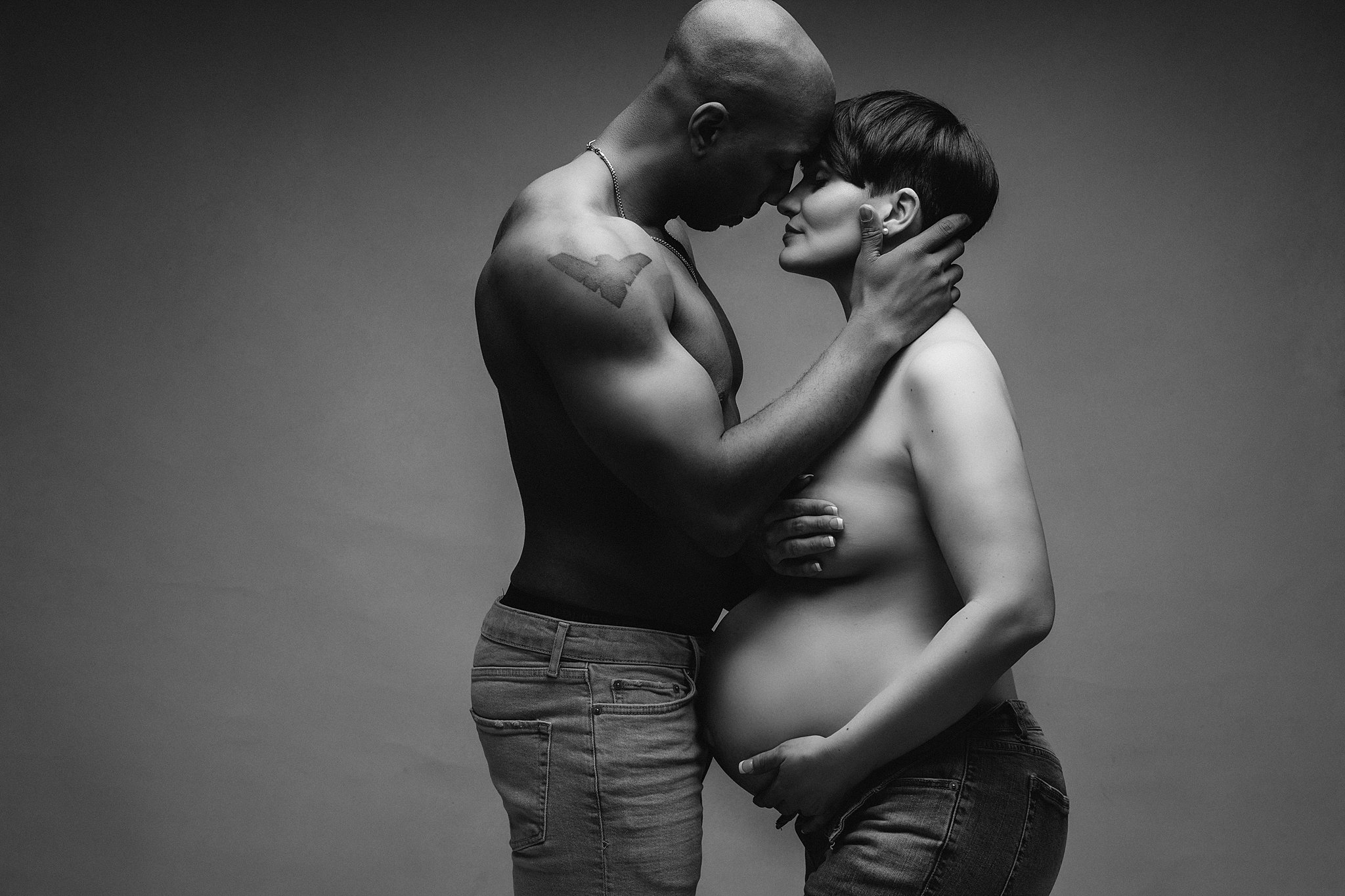 Mother to be stands in a studio with her partner both in jeans athens midwives
