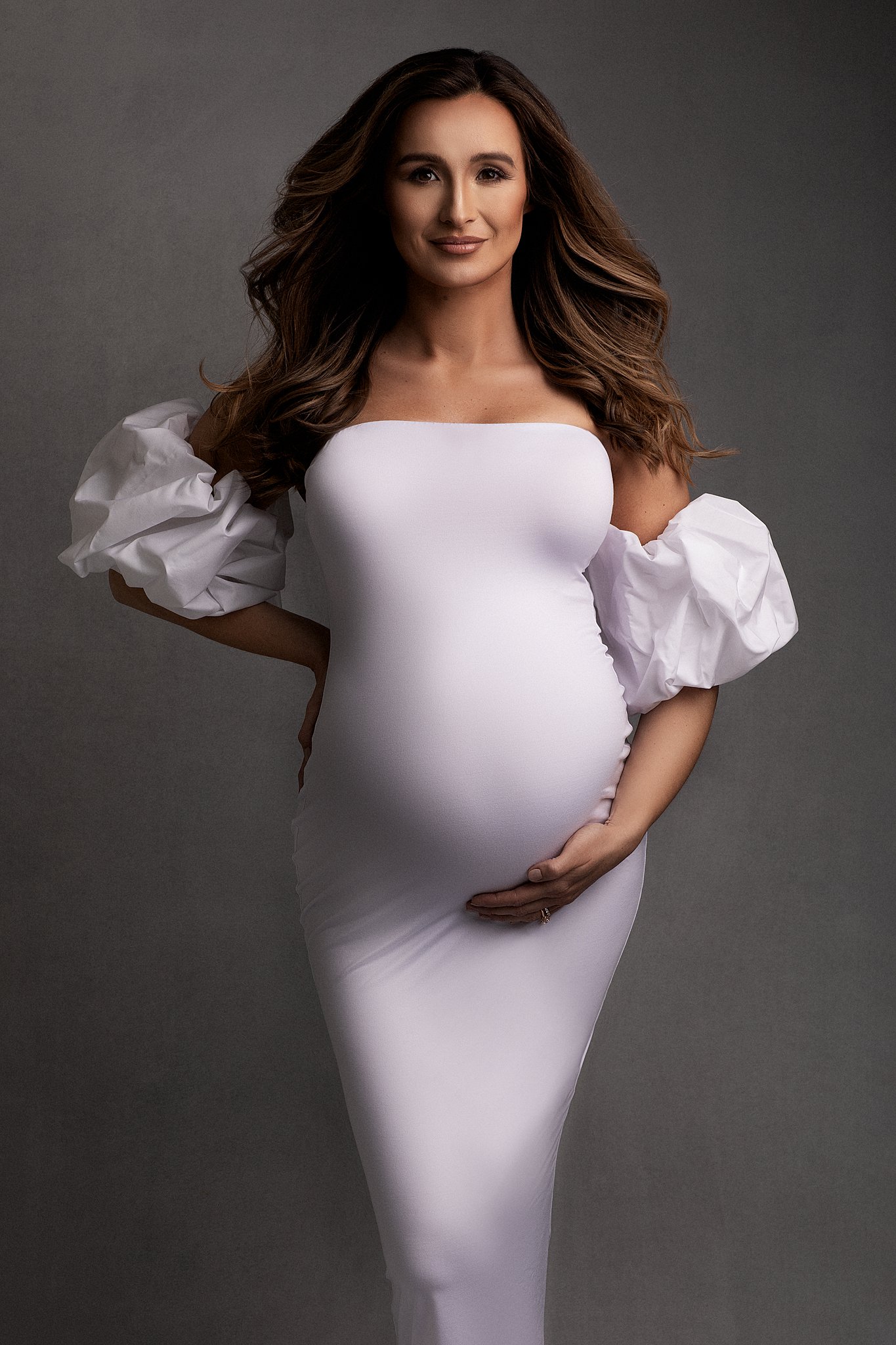 Mother to be stands in a studio in a white maternity gown atlanta baby shower venue