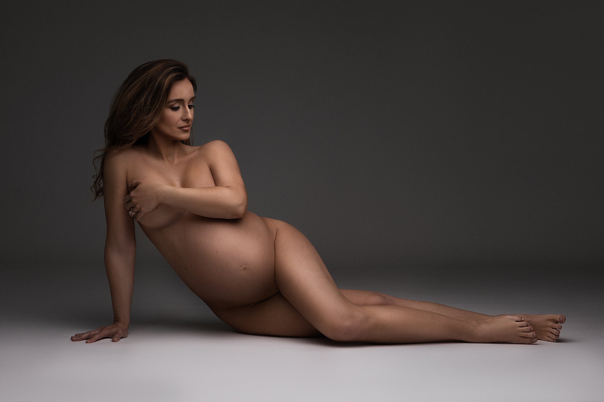 Naked mother to be covers herself with on arm while layin on a studio floor atlanta baby shower venue