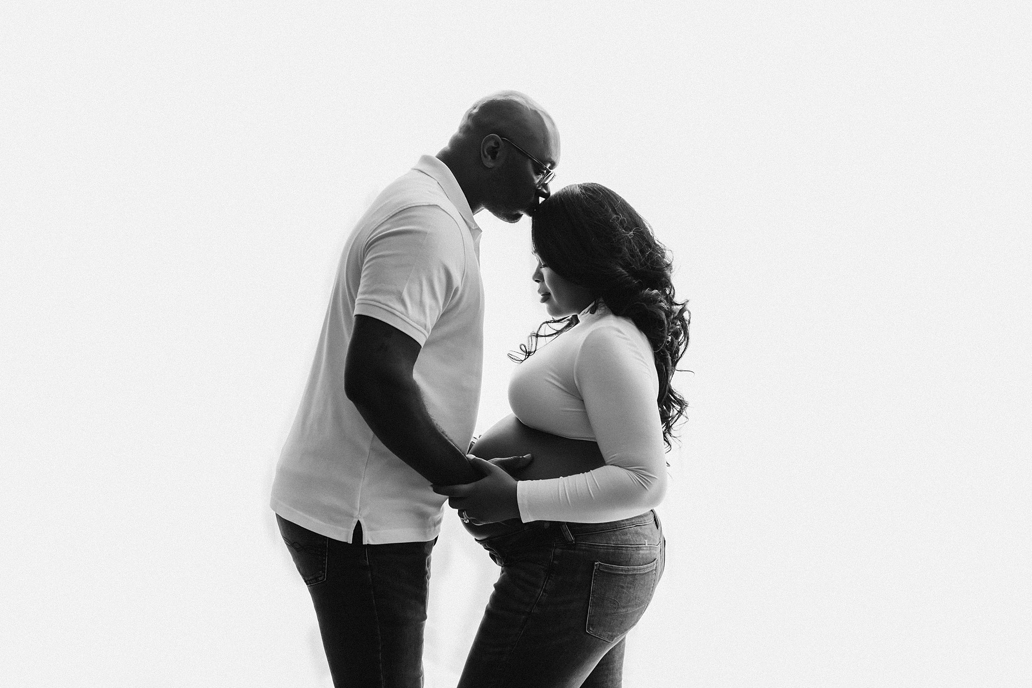 Husband kisses his pregnant wife on the forehead while holding her bump birth by grace midwifery
