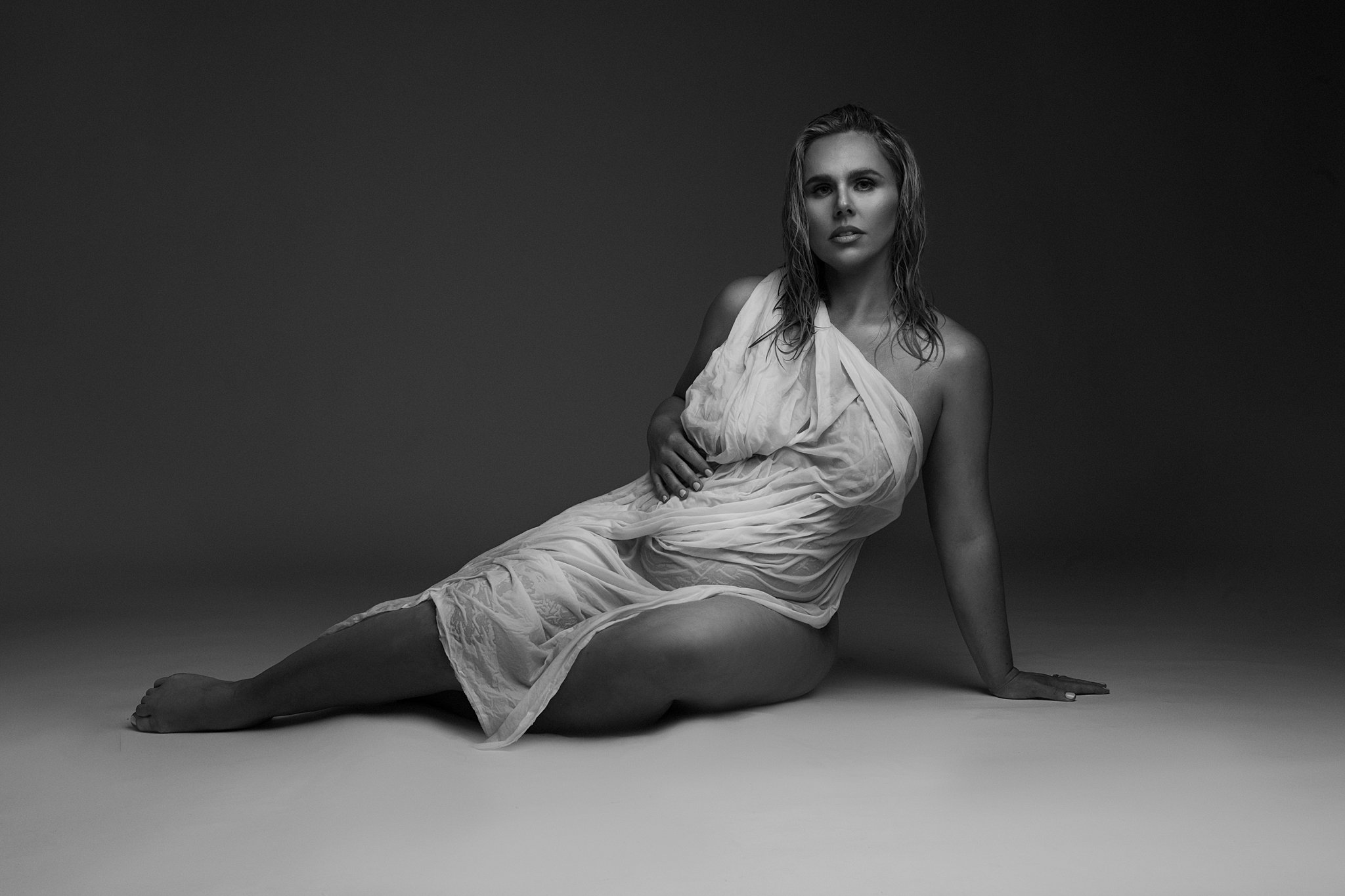 A pregnant woman with wet hair sits on the floor of a studio with a wet sheet draped across her Pregnancy massage center