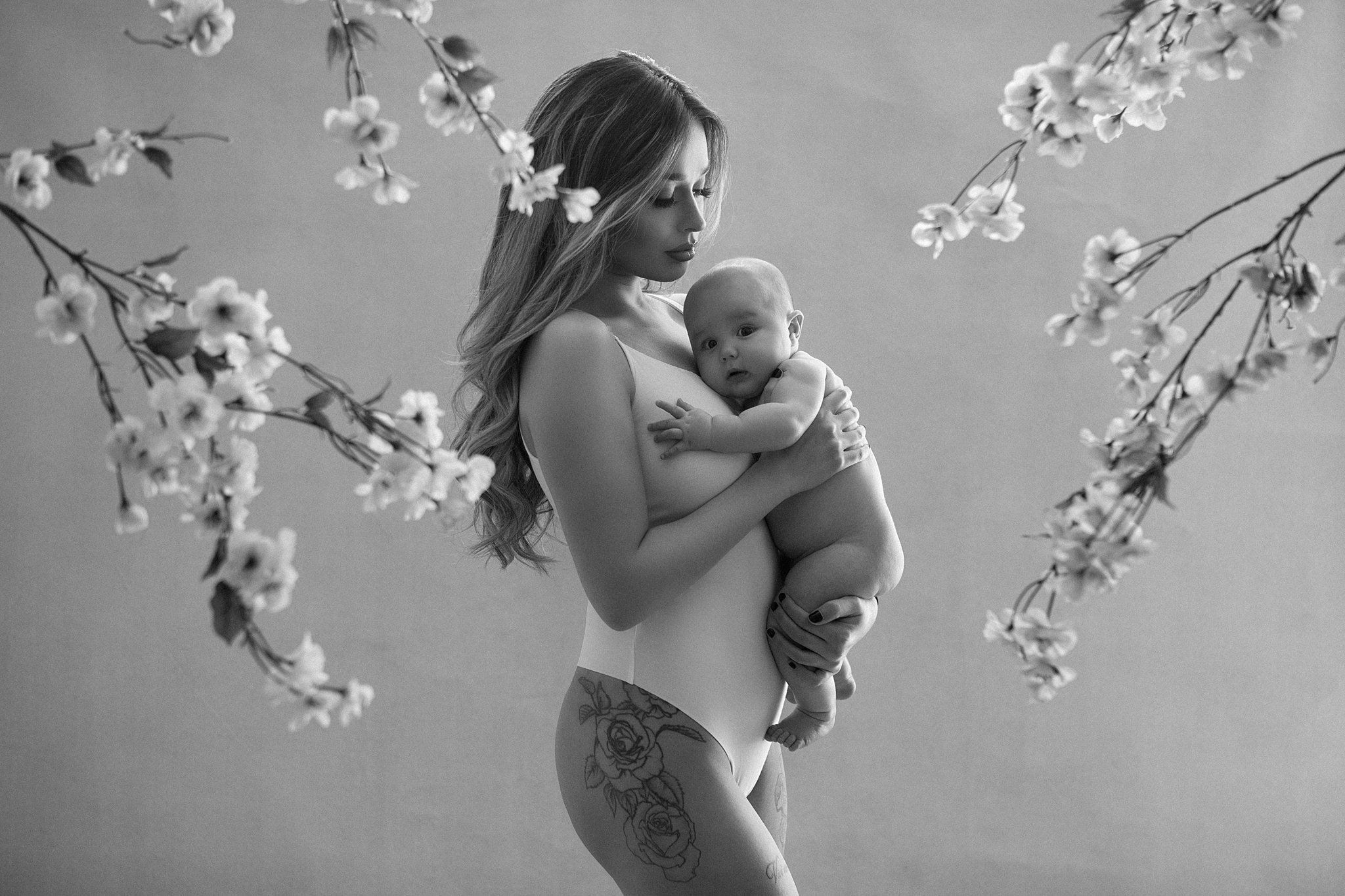 A mother in a white one piece suit holds her young baby on her chest in front of cherry blossoms in a studio athens pediatricians