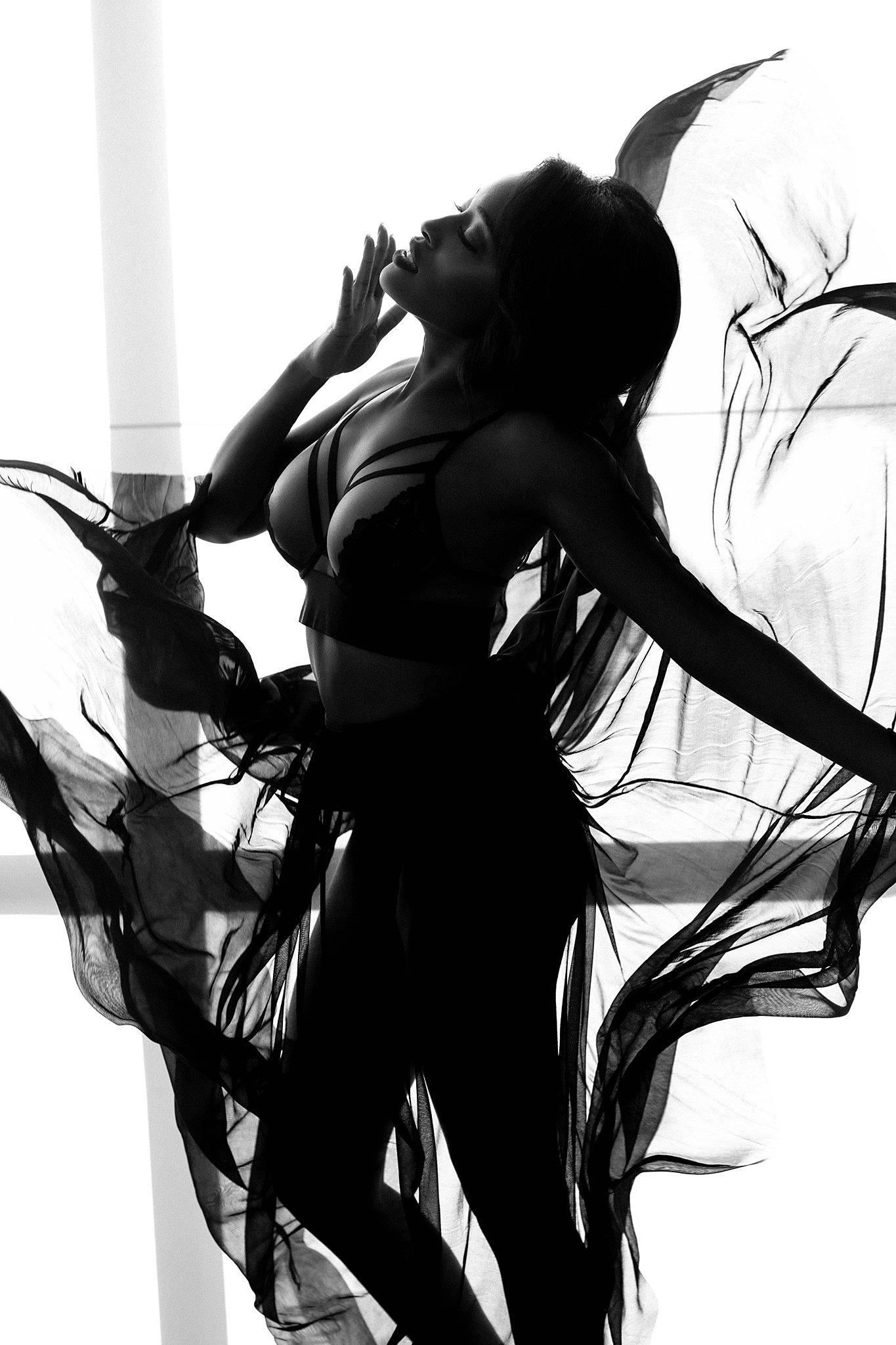 A woman in. black lingerie stands in front of a window with dark sheer fabric flowing all around her bodysense miami