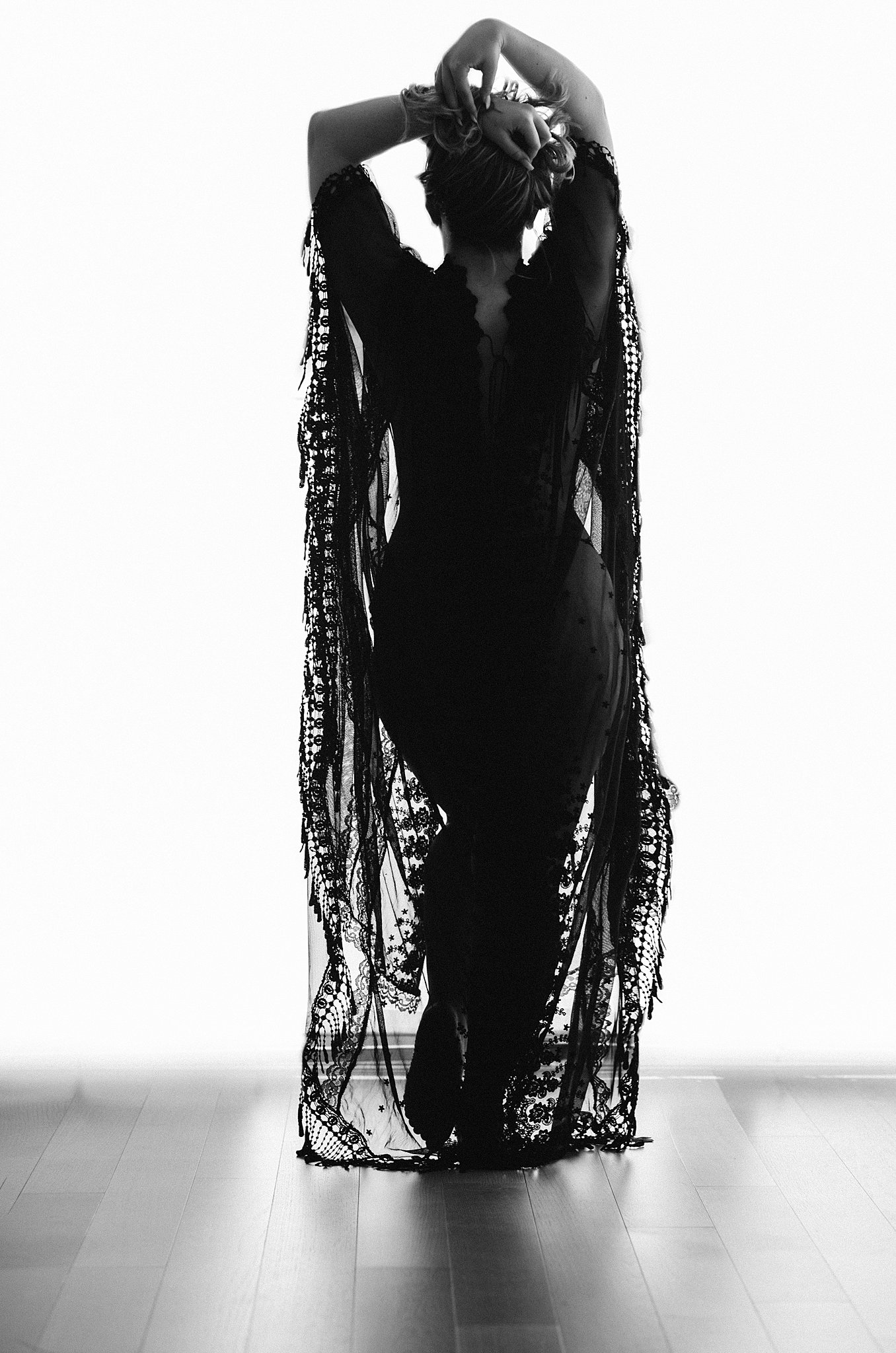A woman stands in a studio wearing a lace coverup holds her hair above her head intimissimi miami
