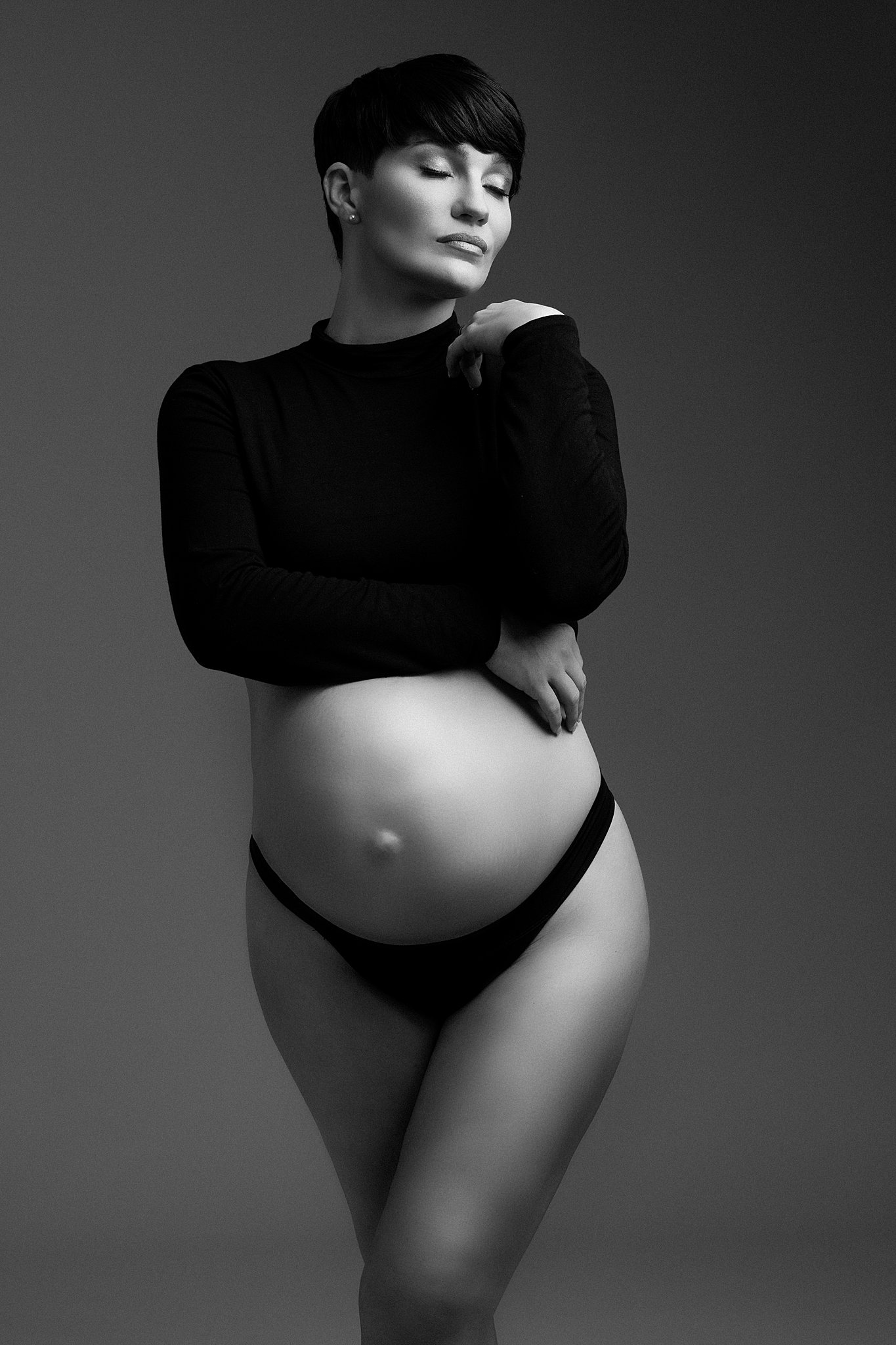 Mom to be stands in a studio in a black long sleeve top that exposes her entire belly moonlight midwifery