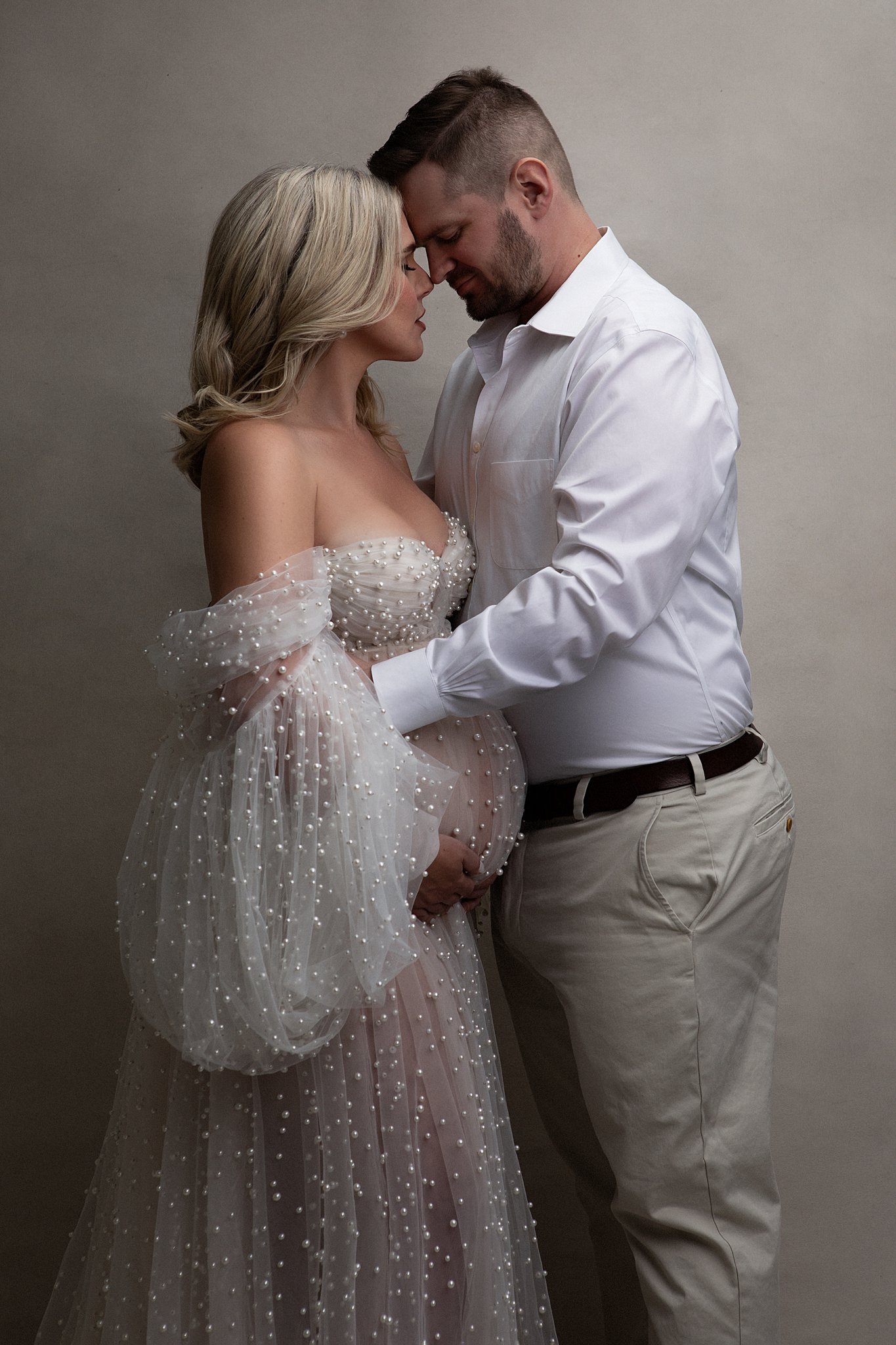 A soon to be father hugs onto his pregnant wife in a sheer maternity gown