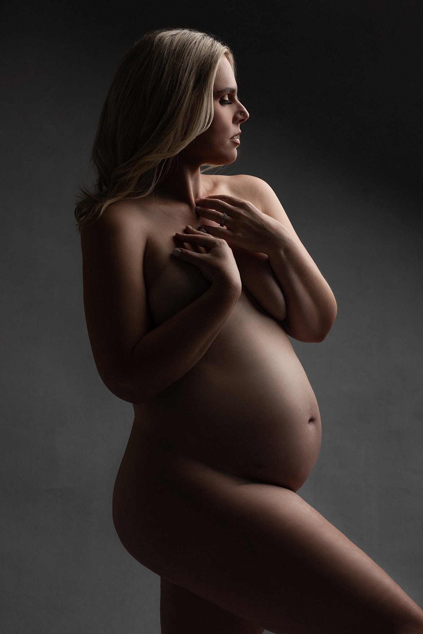 A pregnant woman stands in a studio with long blonde hair