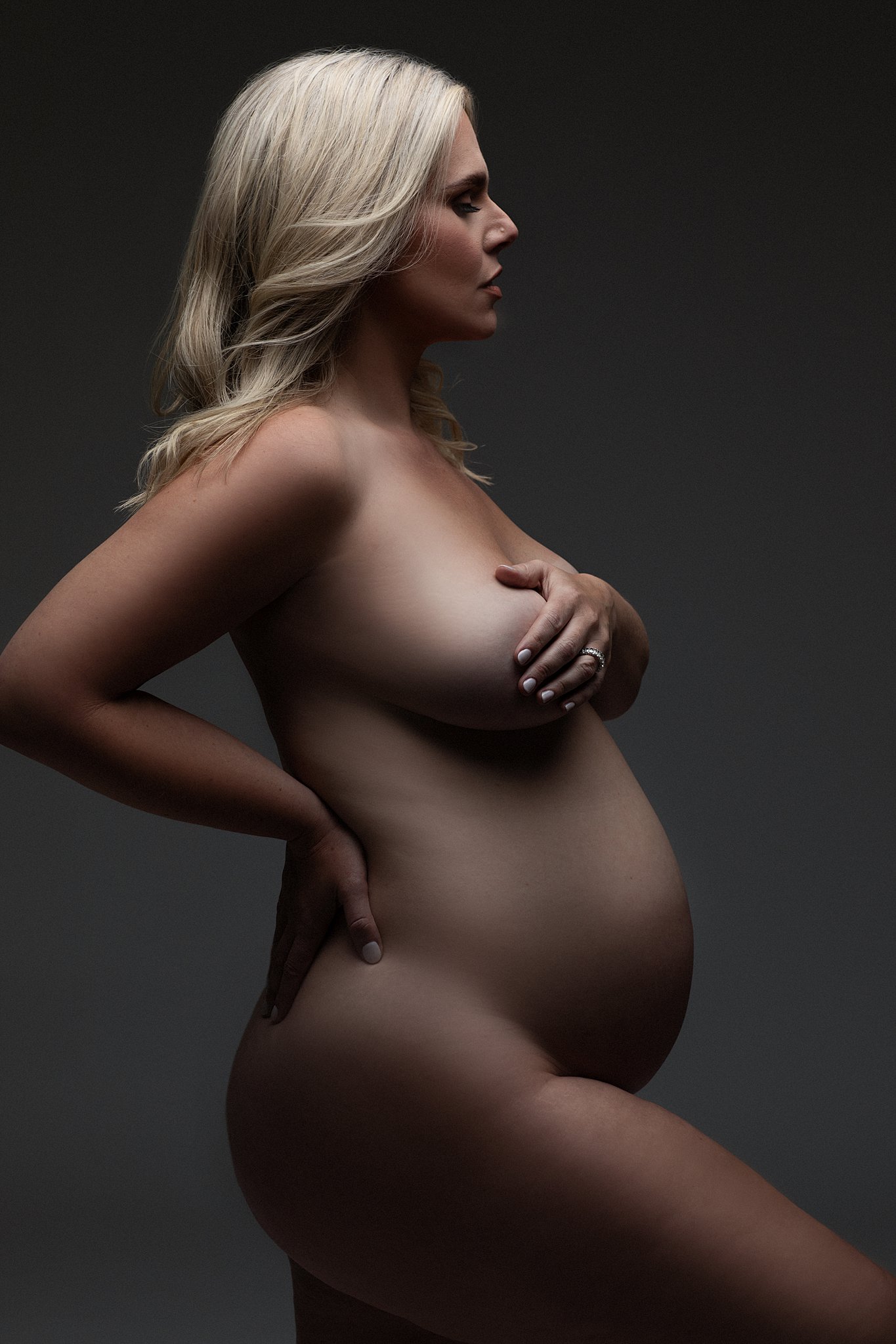 A pregnant woman stands naked in a studio with a hand on her hip and one across her chest miami water birth