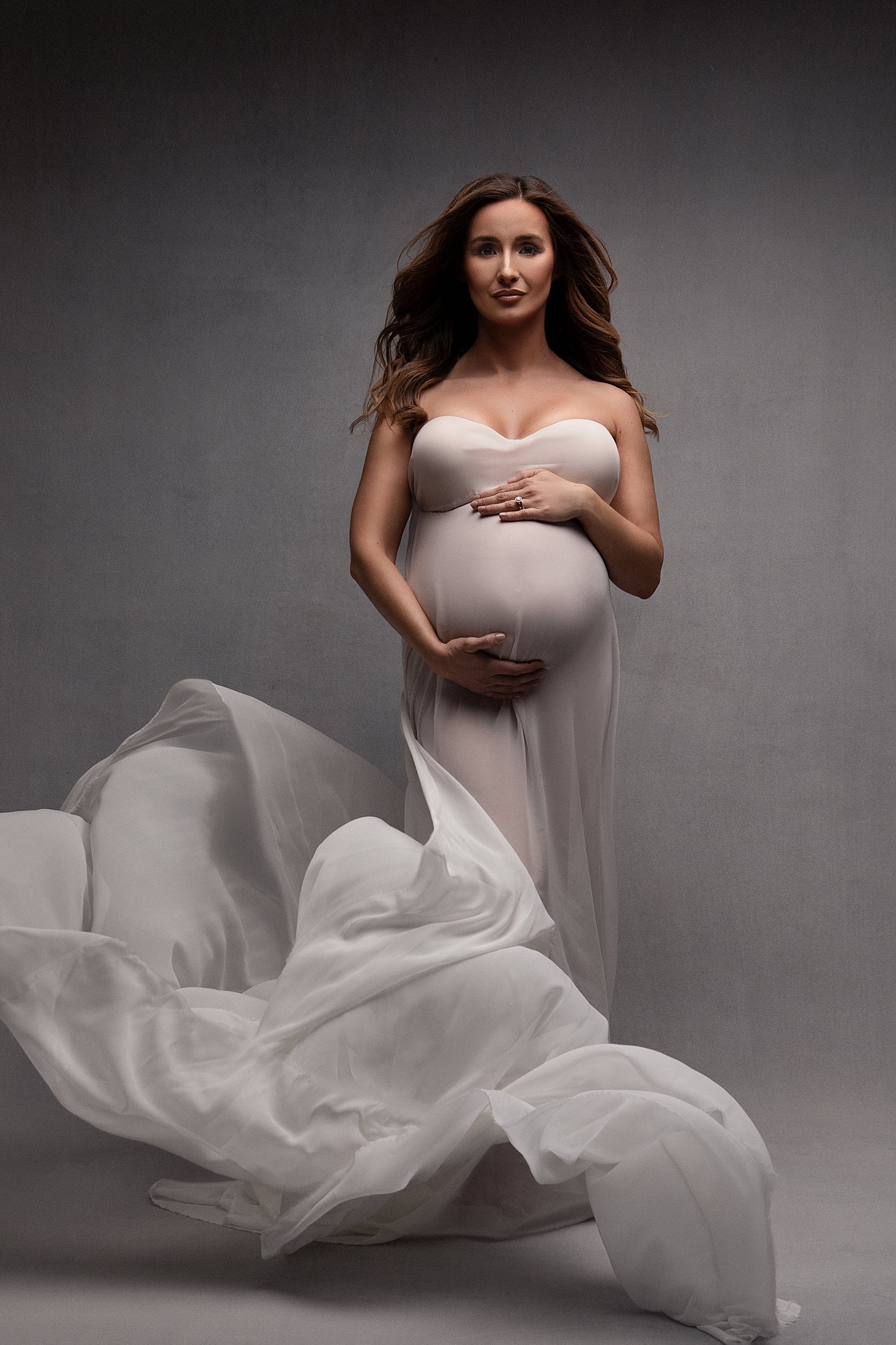 A mother to be stands in a studio covered in a white sheet while it flows around her canton ga pediatricians