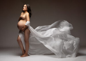 Artistic maternity photo with white sheer fabric billowing behind