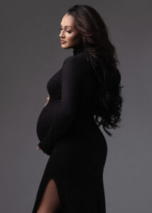 Pregnant woman in black gown holding belly in studio