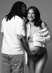 Pregnant couple smiling and embracing in studio with white shirt and jeans