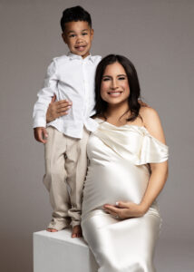 Son standing on white cube beside pregnant mother in satin gown