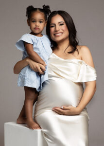 Mother in off-shoulder satin maternity gown holding daughter